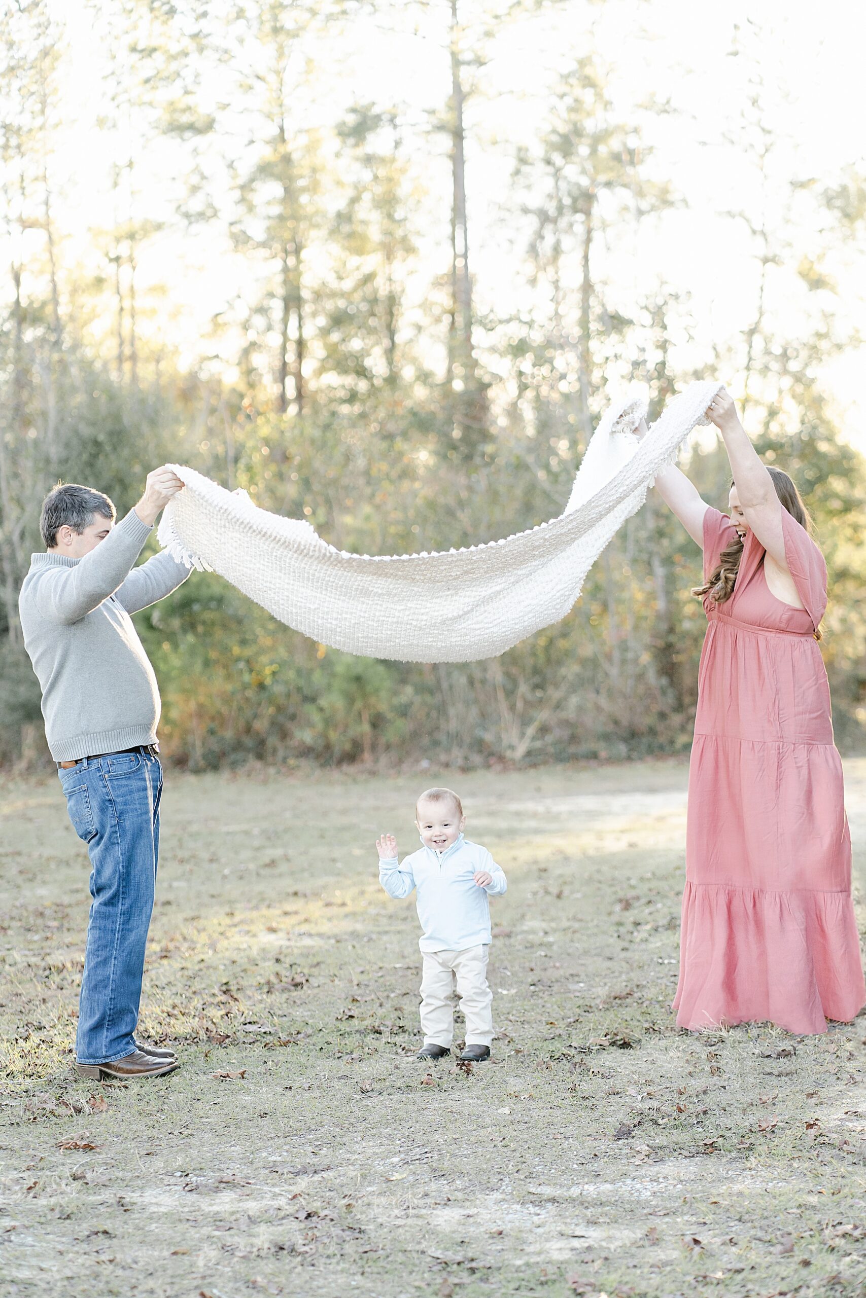 A one year old boy stands playfully under a blanket with his parents during a family session. Photo by Emily Lofton Photography.